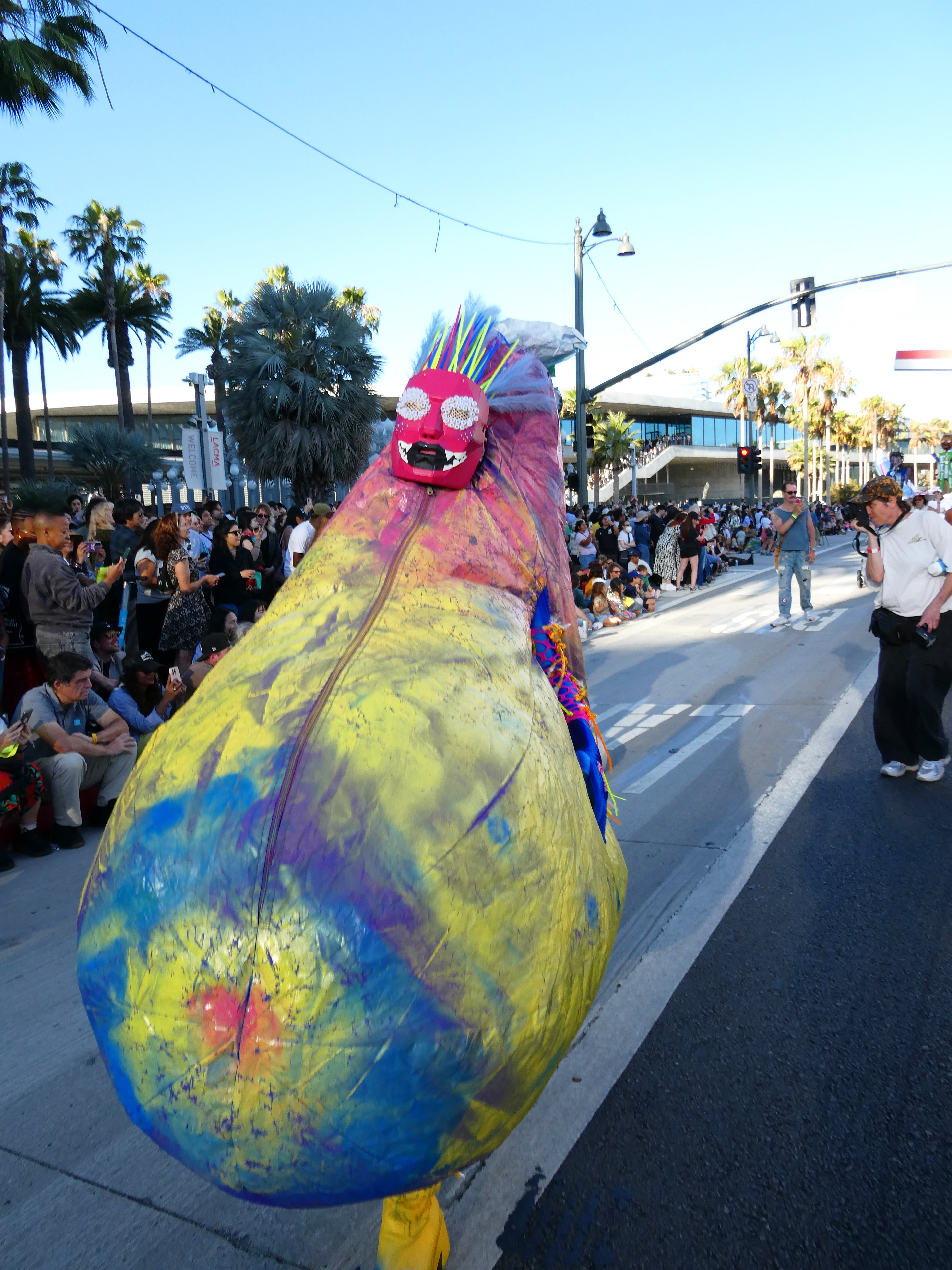 Jesse marching down wilshire boulevard in a Colorful eggplant shaped inflatbale outfit with spectators lining the sidewalk.